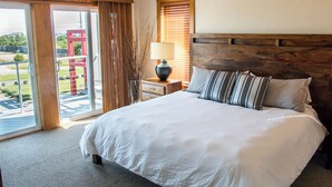 A hotel room with a large bed, a nightstand with a lamp, a view of a red structure through the sliding glass door, and a window with blinds. - 3-Bedroom, 2.5-Bathroom Penthouse Suite at REAL Watersports (Waves)