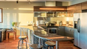 A modern kitchen with stainless steel appliances, a curved island with stools, and a bar area. - 3-Bedroom, 2.5-Bathroom Penthouse Suite at REAL Watersports (Waves)
