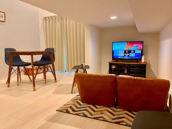 Un salon avec un téléviseur, un canapé, une table à manger avec des chaises et une fenêtre avec des rideaux.