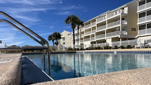A swimming pool with a metal ladder, surrounded by a fence, and adjacent to a multi-story building with balconies.