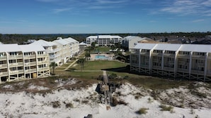 A coastal hotel with multiple-story buildings, a central pool, and a sandy beach area.
