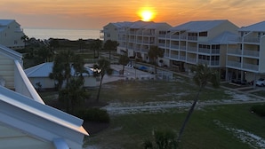 A beachfront hotel with multiple balconies, a swimming pool, and a view of the ocean at sunset.