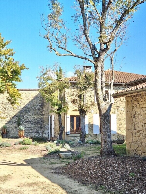 Un edificio de piedra con techo de tejas, rodeado de árboles y un camino de grava.