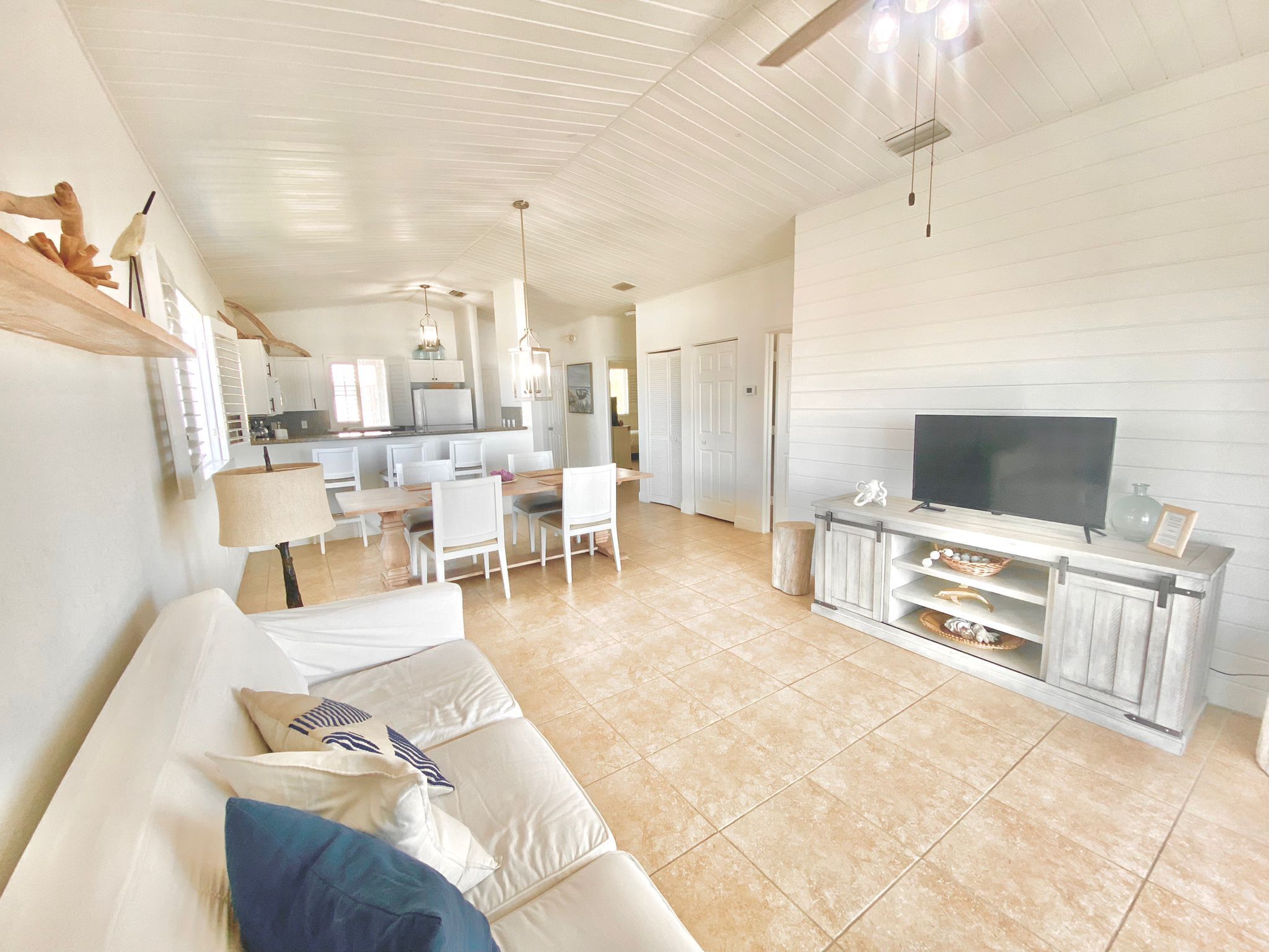 A spacious living area with a white sofa, a dining table, and a kitchen in the background.