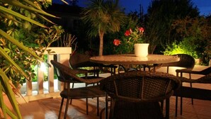 Een terras buiten met rieten meubels, een ronde tafel en een bloempot.