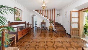 A spacious room with a wooden staircase, a dining area with a table and chairs, and a large vase with flowers. - Finca LHort de Can Bota (Pollensa)