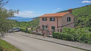Ein zweistöckiges Haus mit rotem Ziegeldach, grünen Fensterläden und Blick aufs Meer.
