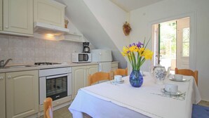 Eine Küche mit Esstisch für zwei Personen, einem Herd, einer Mikrowelle, einem Backofen und einer Vase mit Blumen.