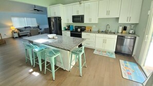 A modern kitchen with white cabinets, a granite countertop, and a central island with bar stools. - Floridays Vacation Home with Pool near to beach by RedAwning (St. Augustine)