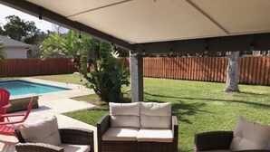 A covered patio area with wicker furniture and a pool in the background. - Floridays Vacation Home with Pool near to beach by RedAwning (St. Augustine)