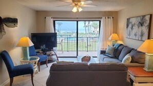 Ein Wohnzimmer mit Sofa, Sesseln, einem Fernseher und einem Balkon mit Blick.