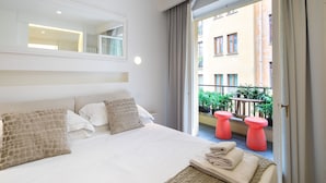 Habitación de hotel con una cama grande, un espejo encima y un balcón con taburetes rojos y plantas.