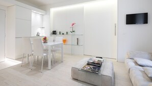 Una sala de estar moderna y minimalista con una mesa de centro de vidrio, un sofá y un televisor de pantalla plana montado en la pared.