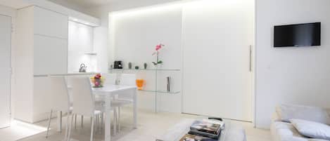 Una sala de estar moderna y minimalista con una mesa de centro de vidrio, un sofá y un televisor de pantalla plana montado en la pared.