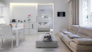 Una sala de estar moderna con un sofá, una mesa de centro y un televisor. Hay una zona de comedor con sillas y una mesa.