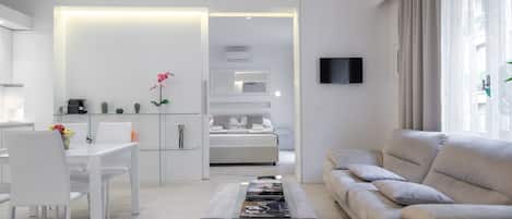 Een moderne woonkamer met een bank, een salontafel en een televisie. Er is een eethoek met stoelen en een tafel.
