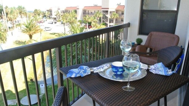 Ein Balkon mit Korbmöbeln, einem Tisch gedeckt mit einem Glas, einer Tasse und einem Teller.