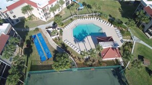 Vista aérea de un complejo residencial con piscina central, sillas de descanso y palmeras.