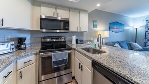 A modern kitchen with stainless steel appliances, a granite countertop, and a built-in dishwasher. - Ocean Village Club D15 New 2 Bedroom Condo by RedAwning (St. Augustine)