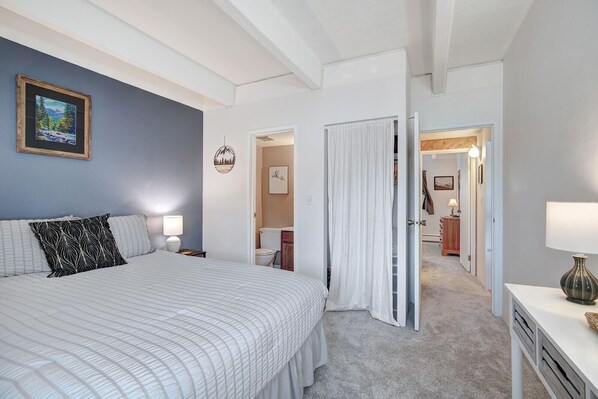 Een slaapkamer met een groot bed, een nachtkastje, een lamp en een schilderij aan de muur.