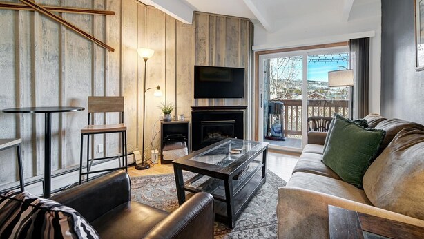 A modern living room with a fireplace, a flat-screen TV, and a balcony with a view. - Ten Mile Creek 304 2 Bedroom Condo by RedAwning (Frisco)