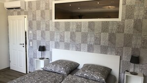 A bedroom with a large bed, a white headboard, patterned wall tiles, a mounted TV, and a door. - Vacation apartments Königsgut Emmericher Eyland (apartment 2) (Kalkar)