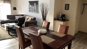 A modern living room with a dining area, featuring a sofa, a coffee table, a dining table with chairs, a lamp, a decorative plant, and a coffee machine on a counter. - Vacation apartments Königsgut Emmericher Eyland (apartment 2) (Kalkar)