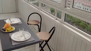 A balcony with a table set for two, a chair, and a view of a cityscape through large windows.