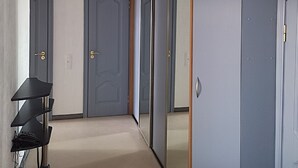 A hallway with a black pendant light, grey wardrobe with a mirror, and a small table with a chair.