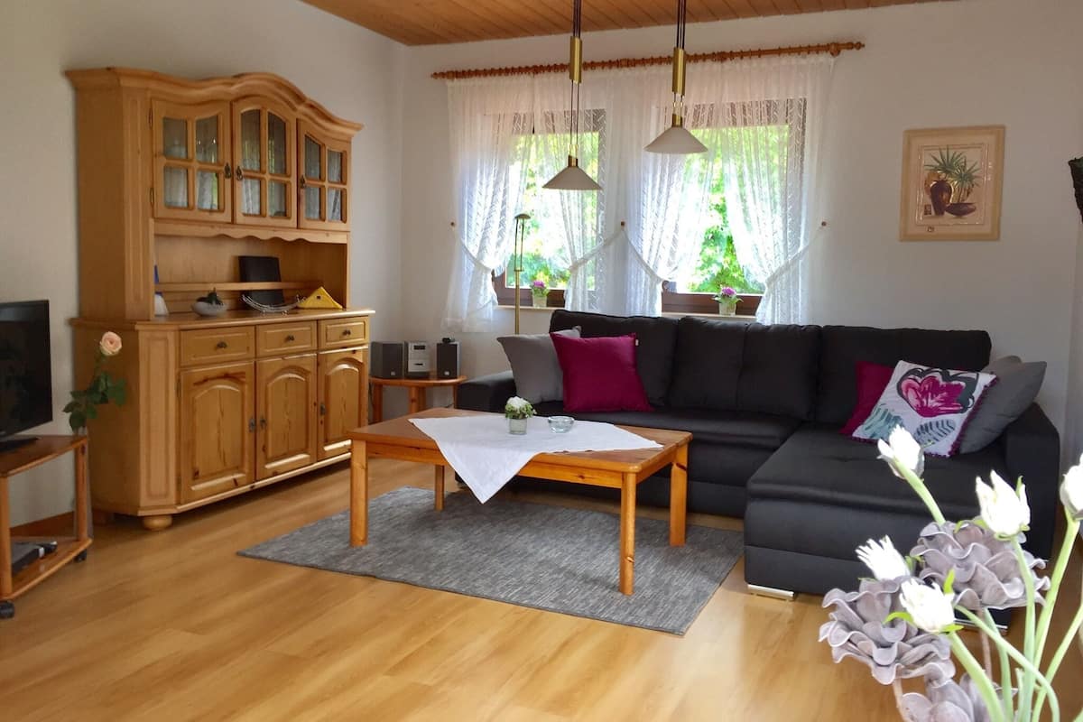 Una sala de estar con un aparador de madera, un sofá negro, una mesa de centro de madera y un televisor sobre un mueble.