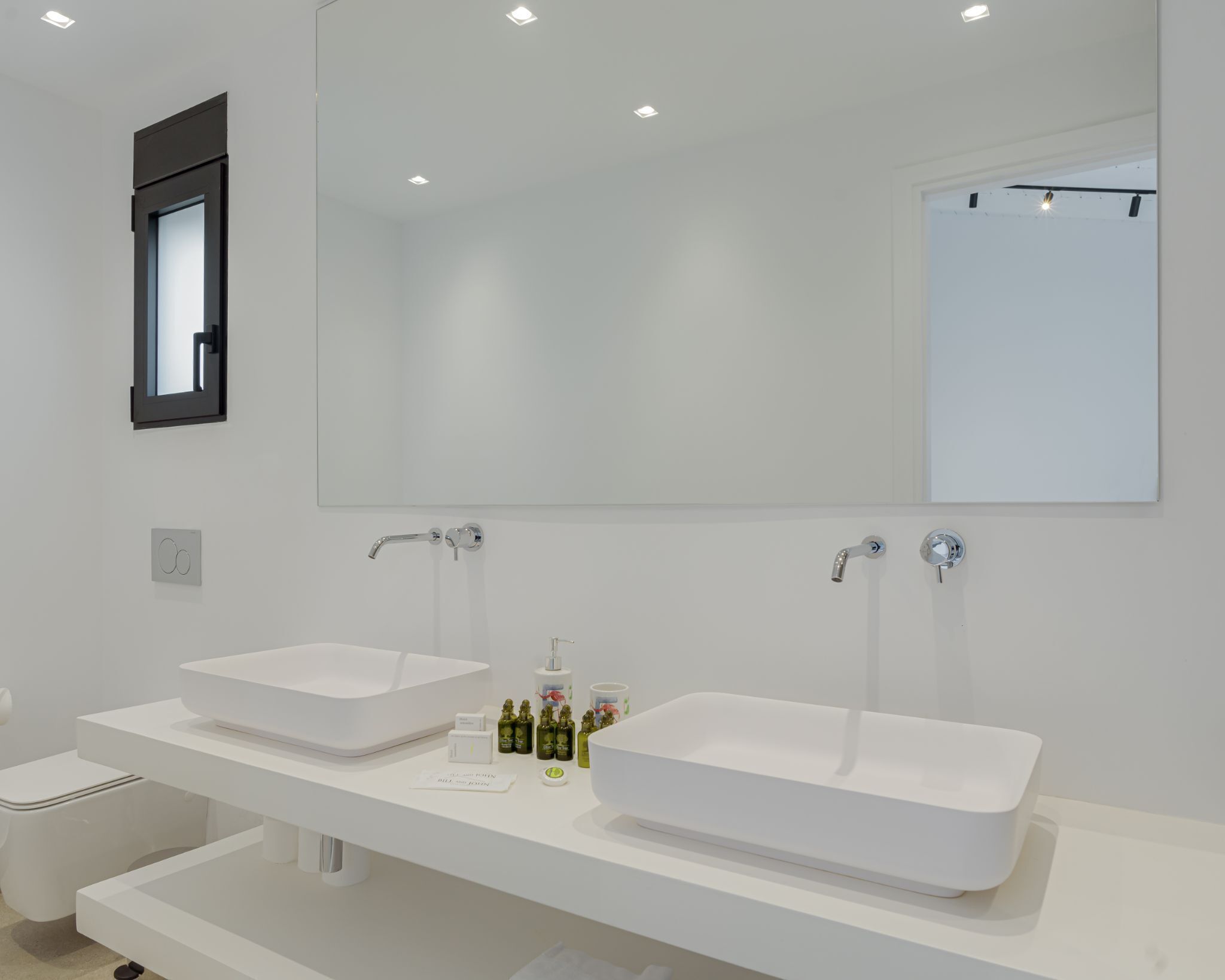 Un baño moderno con dos lavamanos blancos, un espejo grande y un inodoro.
