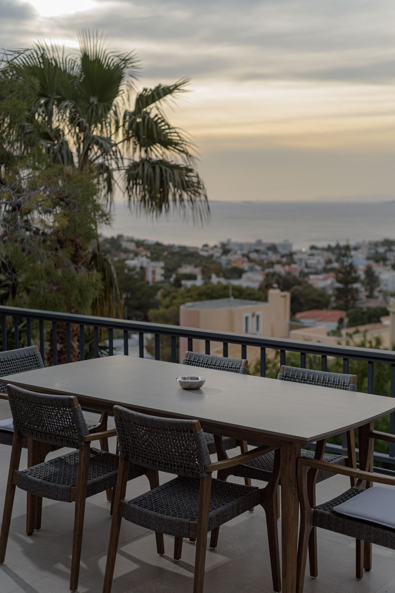 A terrace with a table and chairs, overlooking a coastal town and the sea.