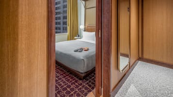 Quarto de hotel com uma cama, uma pequena mesa de cabeceira e uma janela com cortinas.