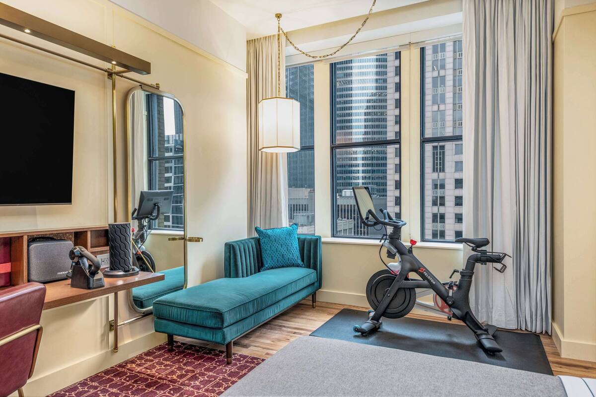 Una habitación de hotel moderna con sofá, bicicleta estática y un ventanal con vistas a la ciudad.