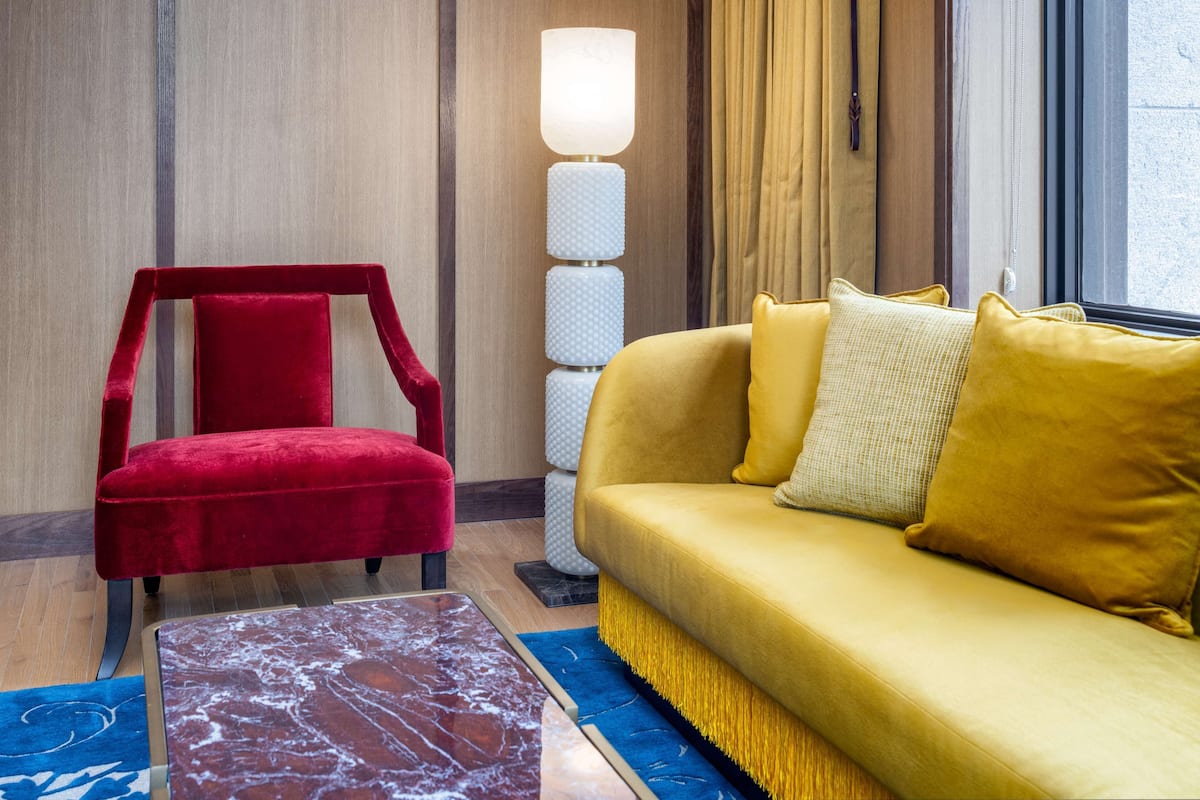 Una habitación con una silla roja, un sofá amarillo, una lámpara de pie y una mesa de mármol.
