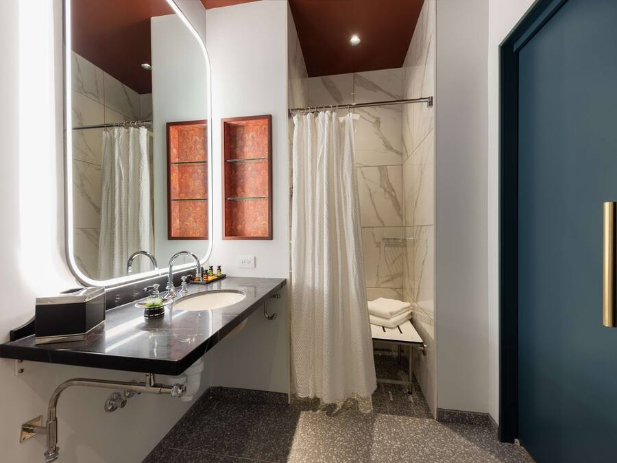 A modern bathroom with a double sink, a large mirror, a shower with a curtain, and a blue door.