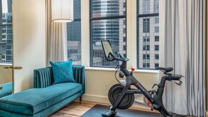 Una habitación moderna con un sofá color turquesa, una bicicleta estática Peloton y vistas a la ciudad a través de amplios ventanales.