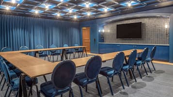Una sala de conferencias con una larga mesa de madera, sillas azules, una pantalla grande y un papel tapiz estampado.