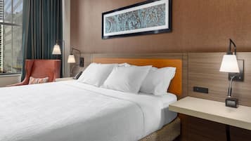 A hotel room with a bed, two bedside lamps, a wall-mounted artwork, and a window with curtains.