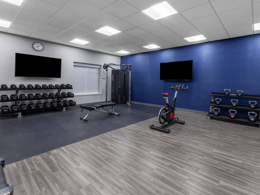 A gym with weightlifting equipment, treadmills, and a wall-mounted TV.