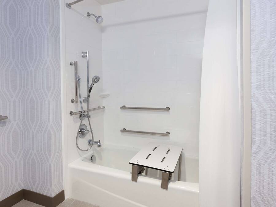 A modern bathroom with a bathtub, shower, and grab bars.