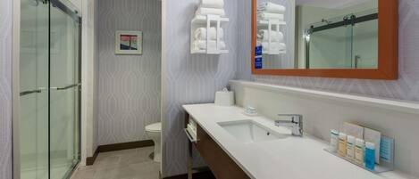 A modern bathroom with a glass shower enclosure, a white sink with a large mirror, and neatly arranged toiletries.