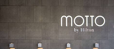 Una pared con el texto "MOTTO by Hilton" y cuatro luces fijadas a ella.