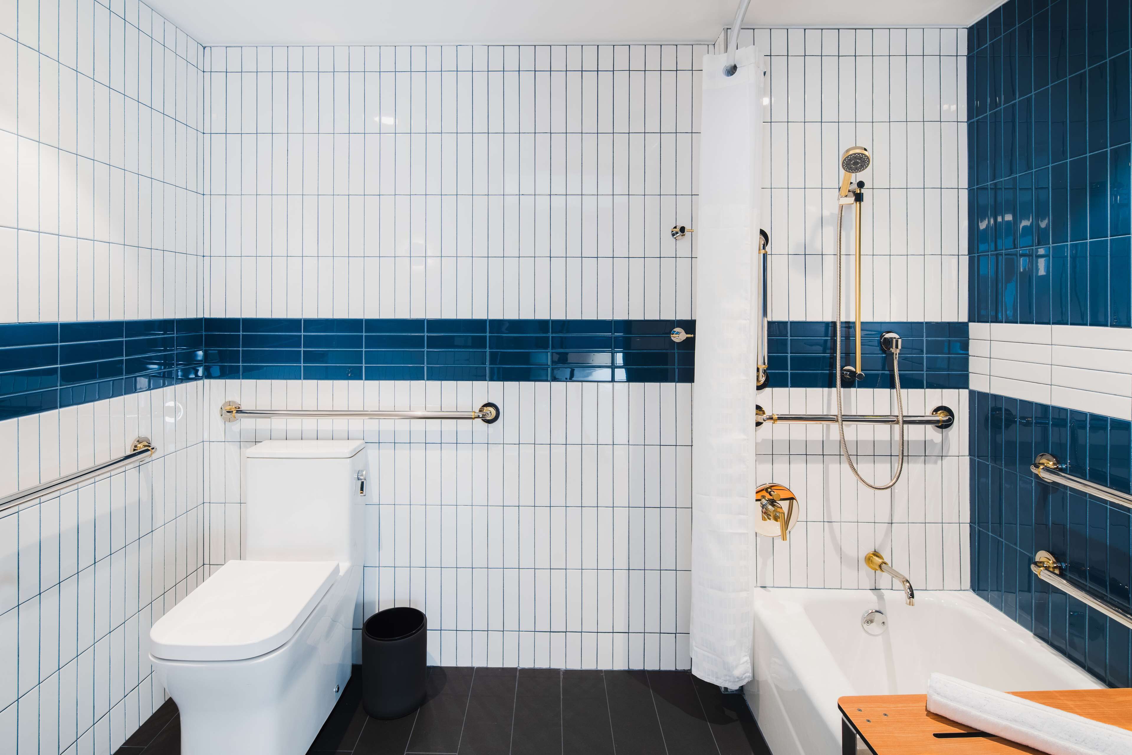 A modern bathroom with a toilet, bidet, and bathtub, featuring blue and white tiles and grab bars.