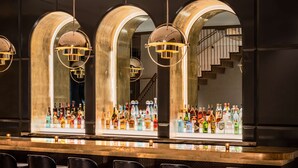 A bar area with a long counter, multiple bottles of liquor, and black bar stools. - Motto by Hilton New York City Chelsea (New York)