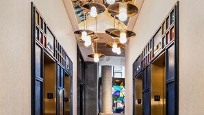 A hallway with black marble flooring, gold elevators, and a ceiling with hanging spherical light fixtures. - Motto by Hilton New York City Chelsea (New York)