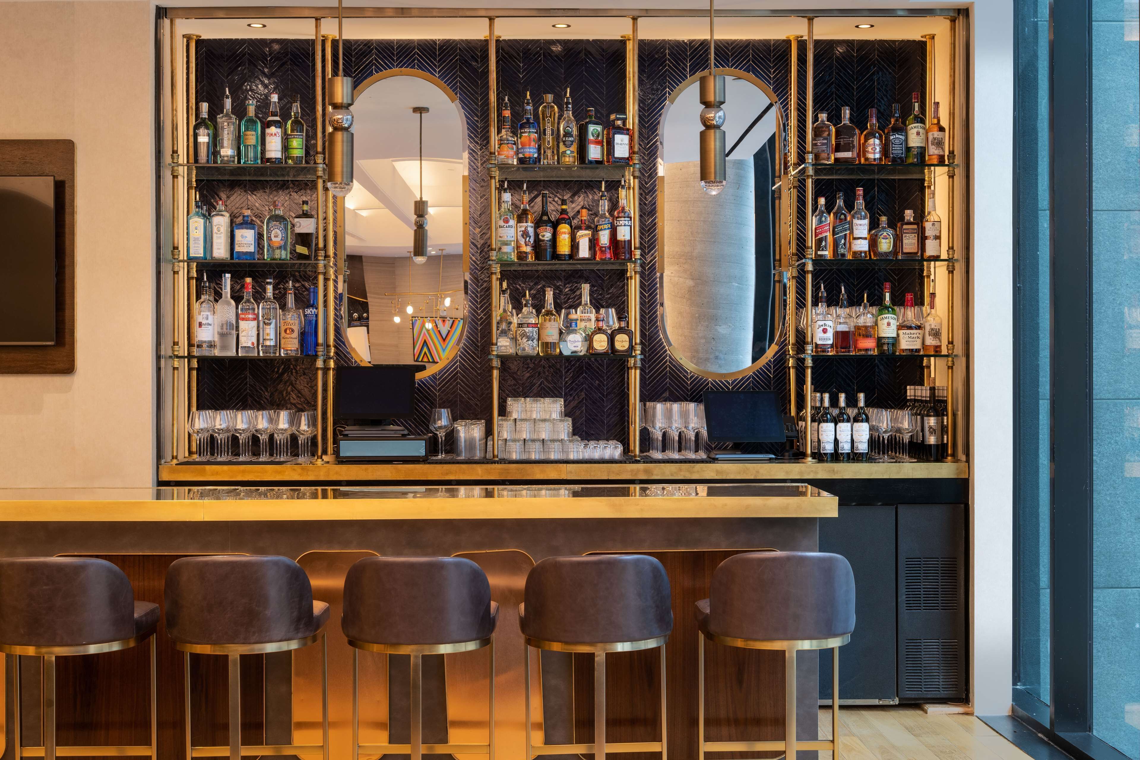 A bar area with multiple shelves of liquor bottles, a mirror, and bar stools.