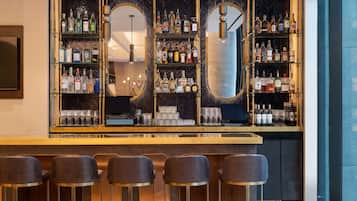 A bar area with multiple shelves of liquor bottles, a mirror, and bar stools.