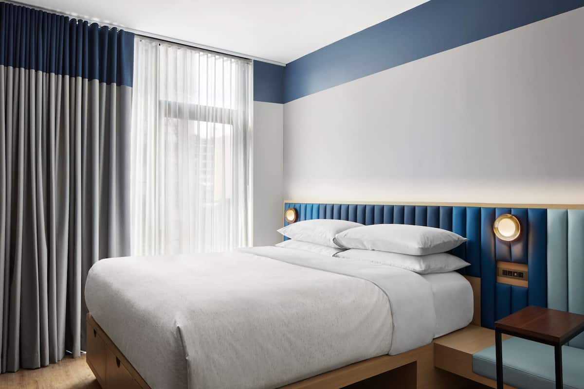 Ein modernes Hotelzimmer mit einem großen Bett, einem Nachttisch und einem Kopfteil mit integrierter Beleuchtung.