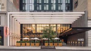 Un edificio moderno con fachada de vidrio, área de estar al aire libre con sombrillas y un interior de restaurante visible.